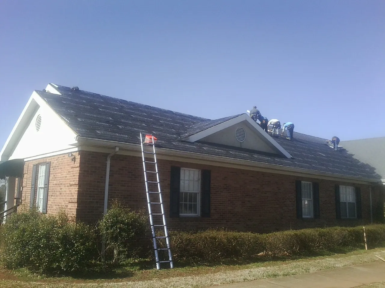 Crew tearing shingles off a brick ranch roof with a ladder set — Emergency Roof Repair work by our crew in Carefree