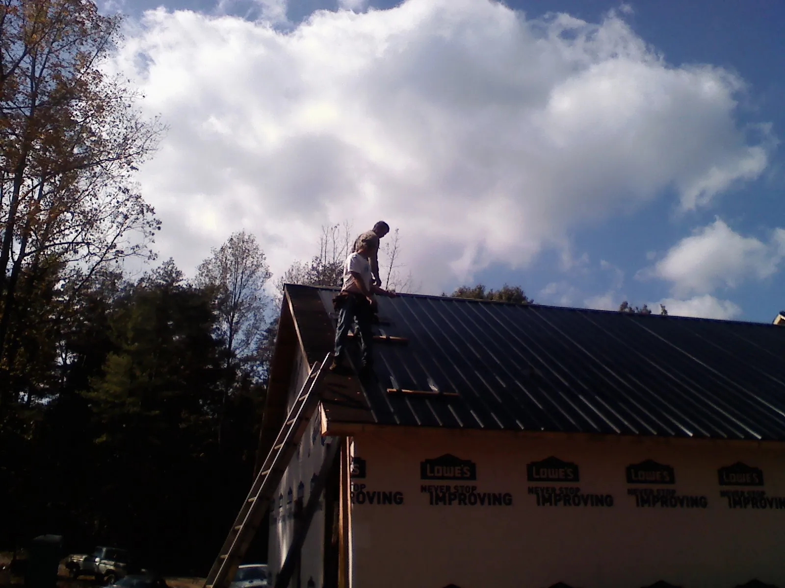 Roofer fastening dark metal panels high against a cloudy sky, from a Roof Inspection job in Carefree